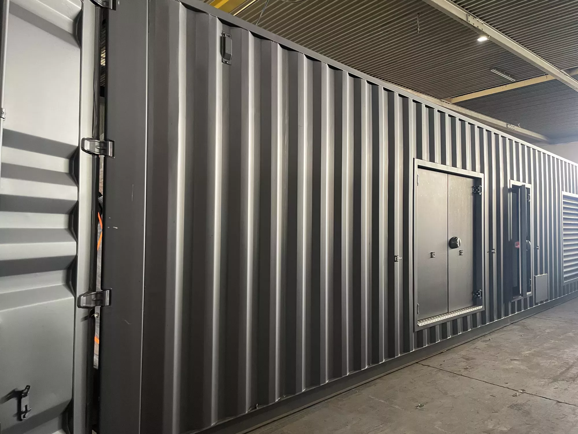 FlexEskid custom container — factory-built corrugated steel enclosure with personnel access doors and ventilation louvres, ready for equipment installation.