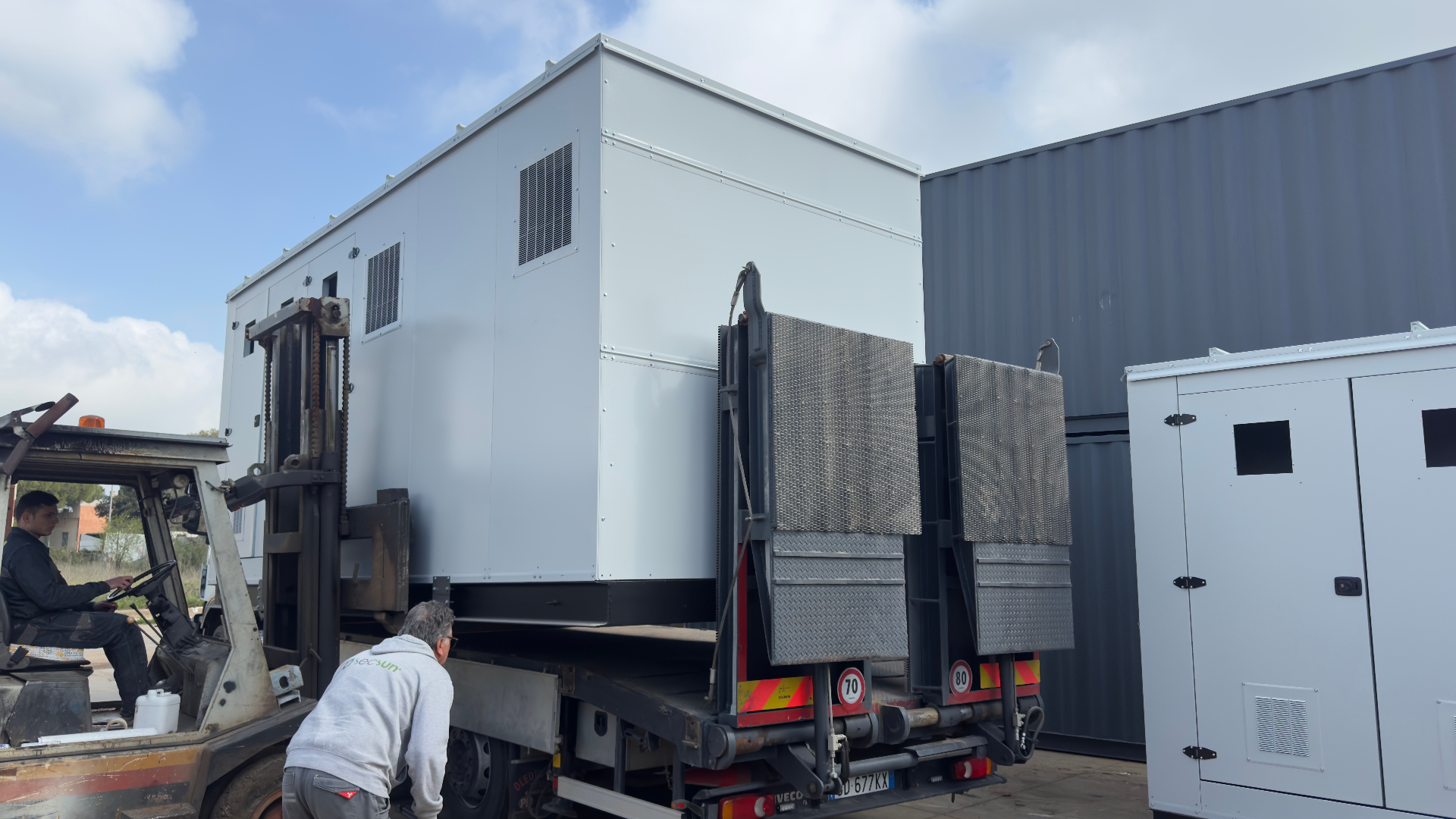 FlexEskid loaded for dispatch — fully assembled enclosure lifted onto a flatbed trailer by forklift, ready for delivery to site.