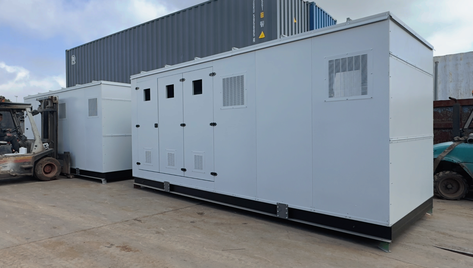 FlexEskid units in the yard — factory-finished acoustic enclosures on structural skid bases with louvred ventilation and multi-door access, ready for dispatch.