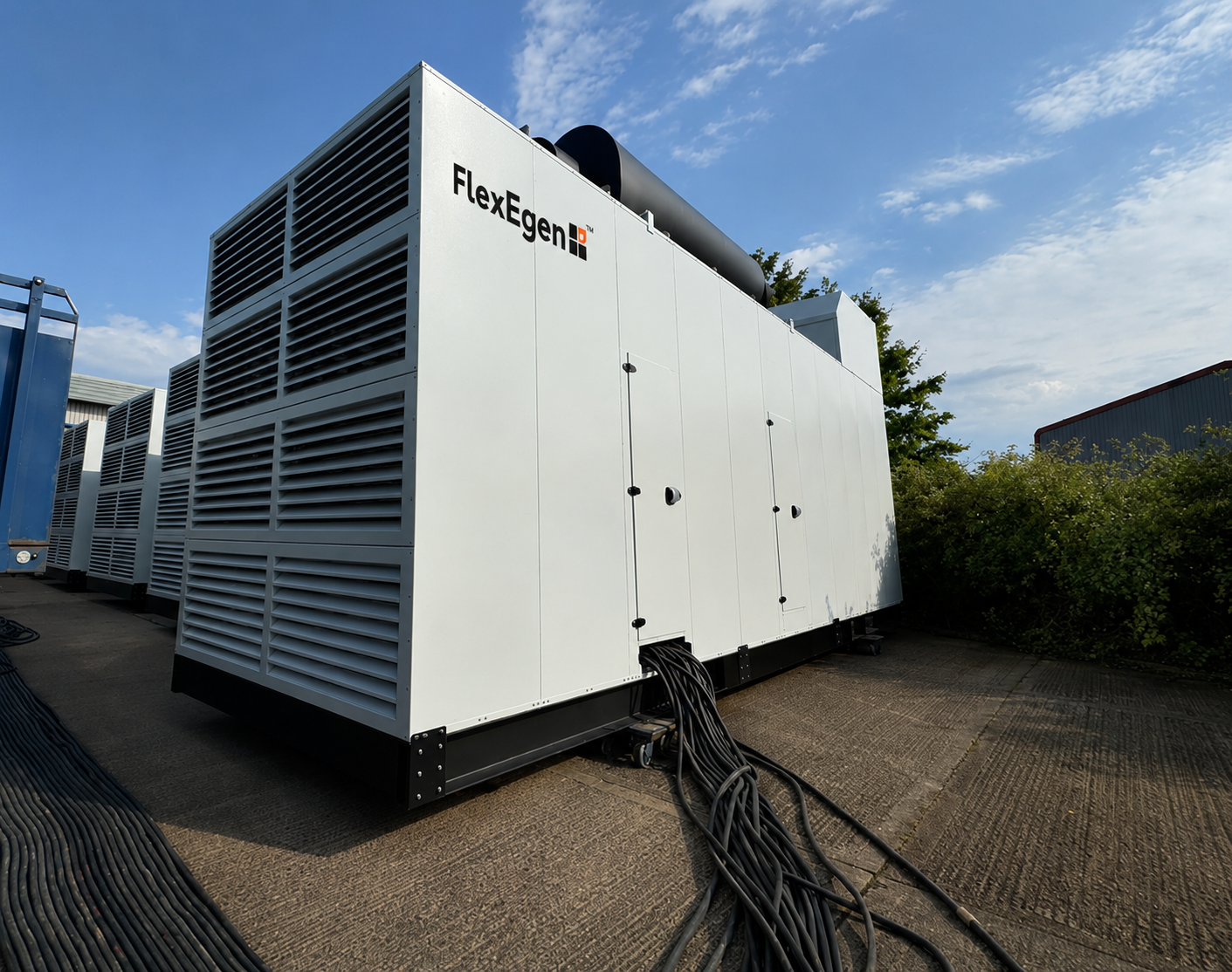 FlexEgen acoustic enclosure on site — branded unit with full-height louvred ventilation, rooftop exhaust silencer and power cable connection.